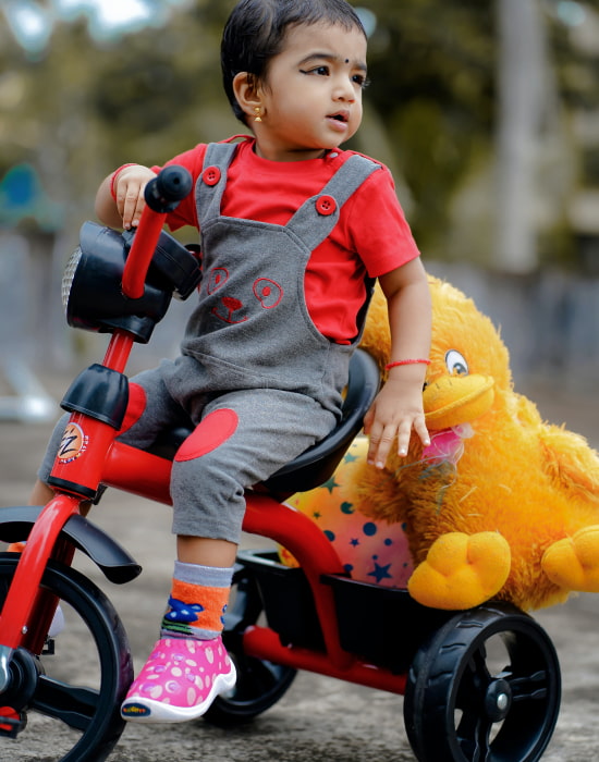 Nesta foto, está uma criança montando em seu triciclo, com seu ursinho de pelúcia e muito feliz.